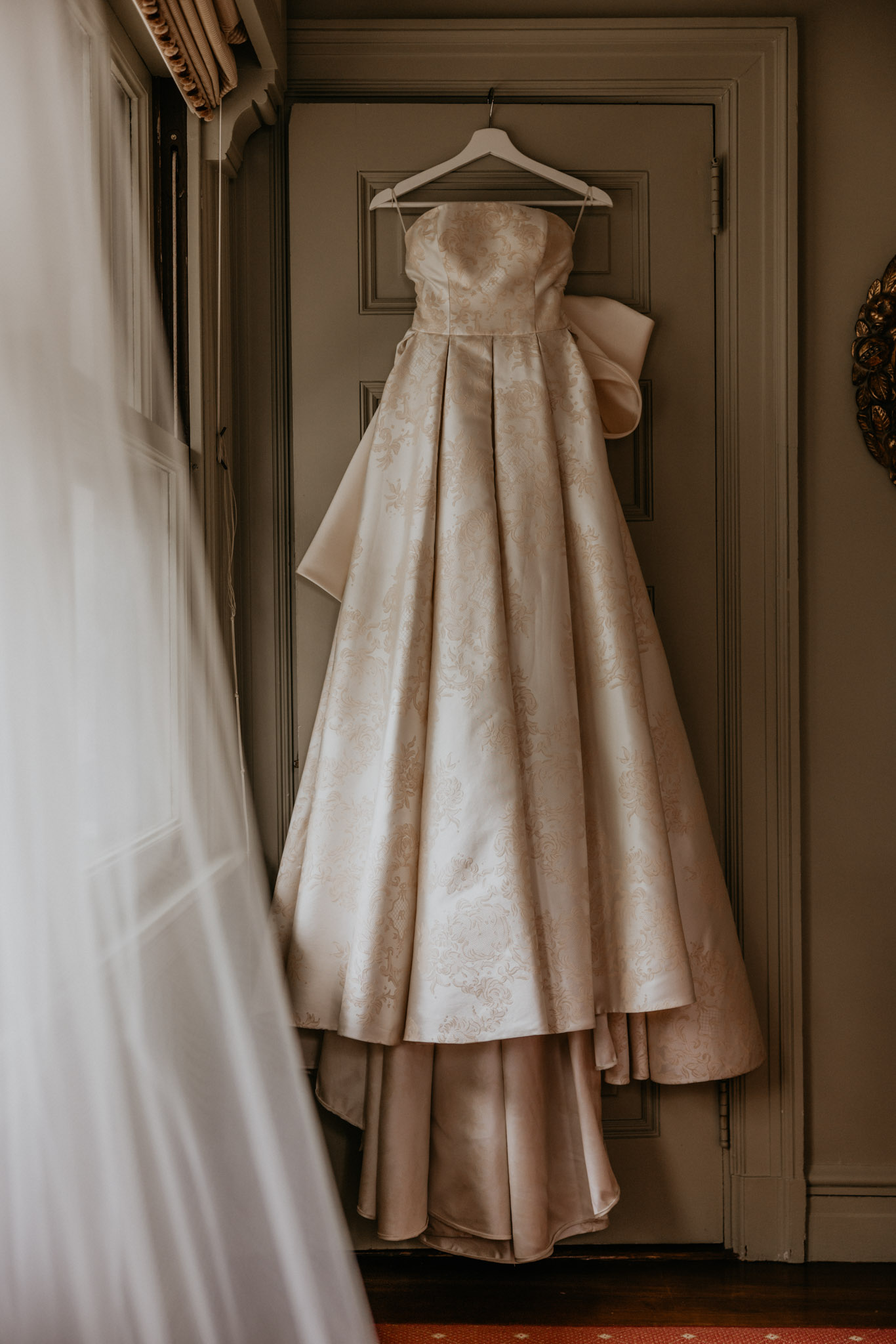 Moody silhouette of a wedding dress hanging against a dark background